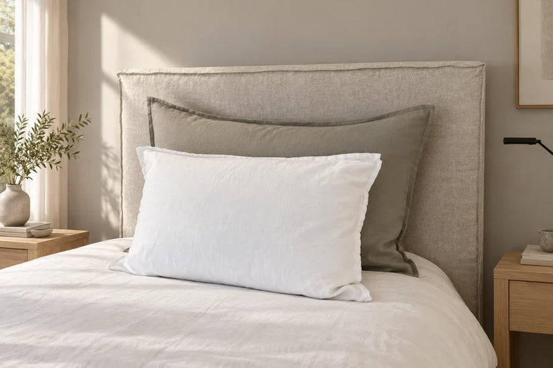 Cama con cojines blanco y verde oliva, ordenados delante de un respaldo beige.